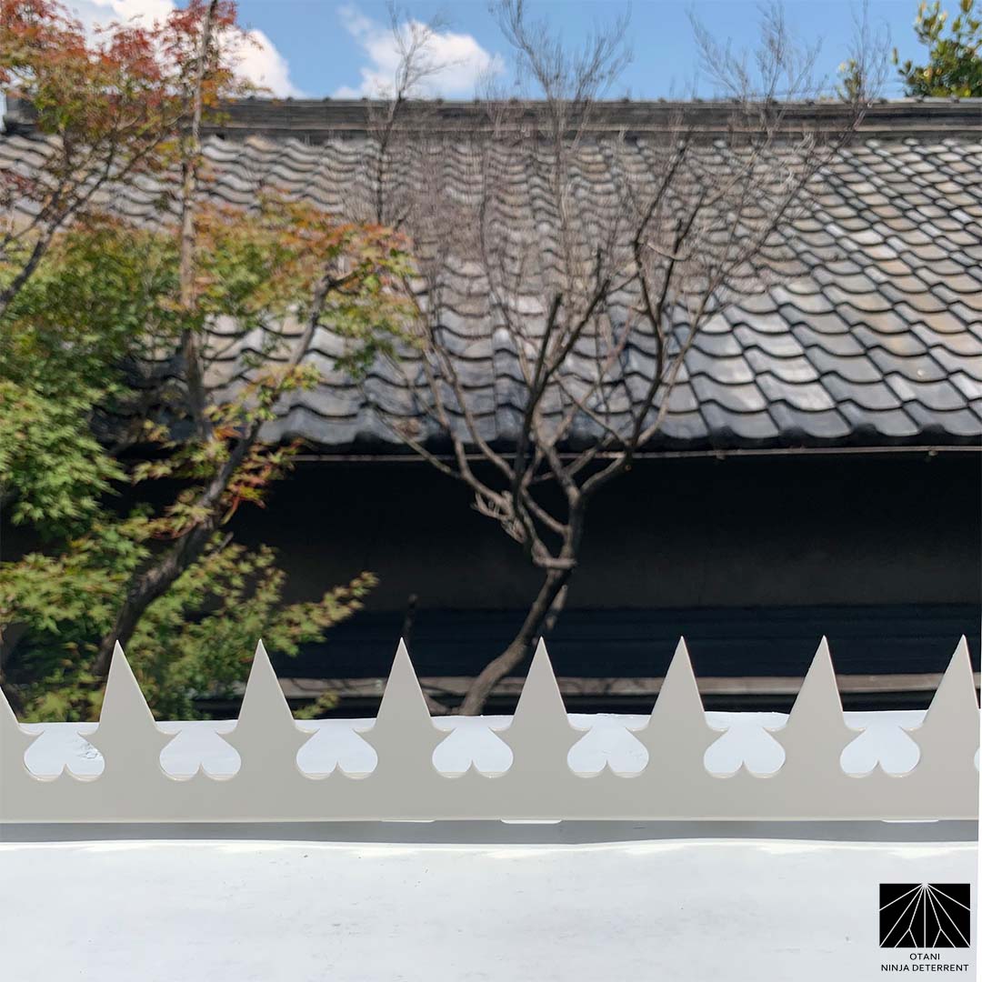 GIZAGIZA heart white installed on white wall with traditional Japanese tile roof – discreet security with cultural harmony